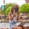 a young woman repositioning her sunglasses as she fits on the edge of a large stone fountain